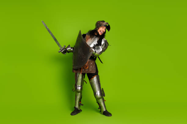 A young man dressed in antique metal armor holding a sword and smiling, standing on a vivid green backdrop. The scene exudes a blend of history and fun.