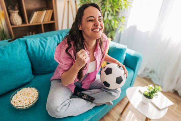 istock Excited young woman cheering while watching soccer game on tv 2203209481
