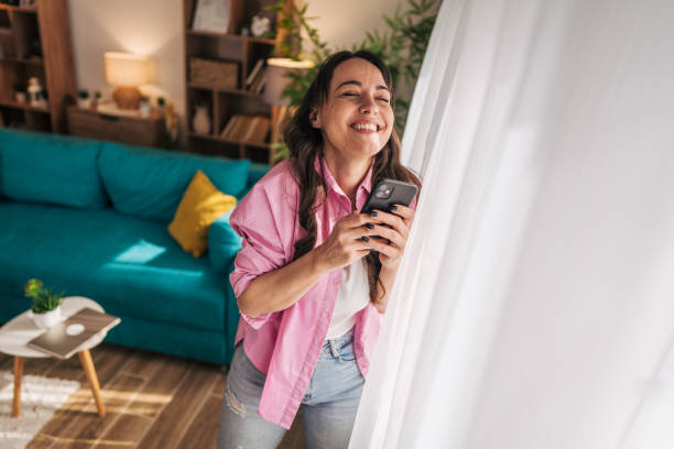 istock Happy woman enjoying sunlight and using smartphone at home 2203209732