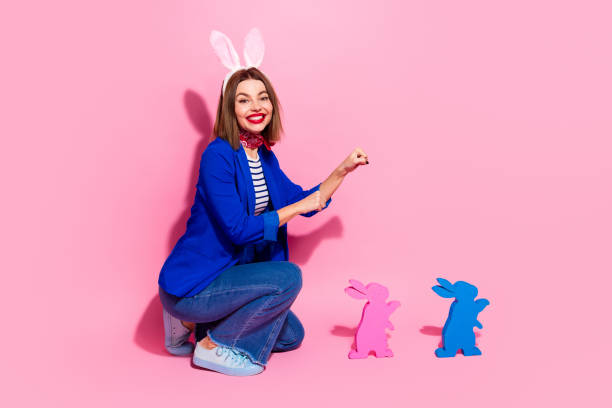 istock Happy young woman in blue jacket and bunny ears playing with colorful Easter decorations on a pink background 2203211714