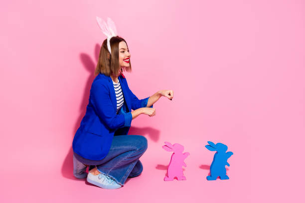 istock Young woman with bunny ears posing stylishly in a blue blazer, surrounded by decorative rabbit figures on a vibrant pink background. 2203211736
