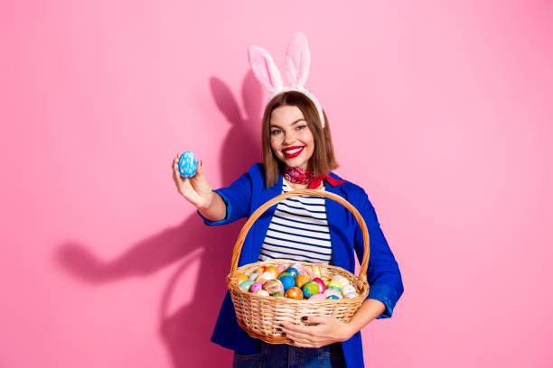 istock Young woman with bunny ears holding Easter egg basket against pink background celebrating holiday in cheerful mood 2203211780