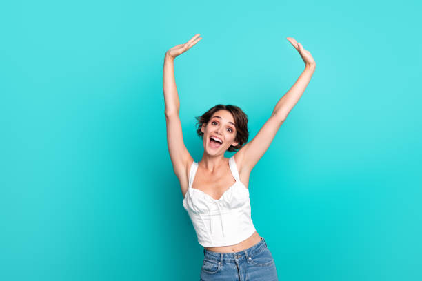 istock Cheerful young woman in a white top gesturing joyfully on a turquoise background emphasizing happiness and vibrant energy 2203216041