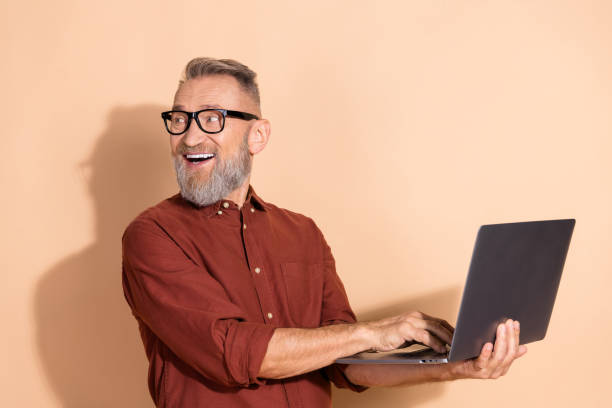istock Smiling mature man with laptop represents positivity, business ambition, and modern professional lifestyle on a beige background. 2203216511