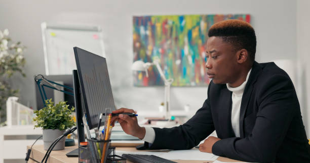 istock Focused mixed-race businessman compares paper graphs with digital charts, signs documents, and verifies data accuracy at his desk. 2203217637