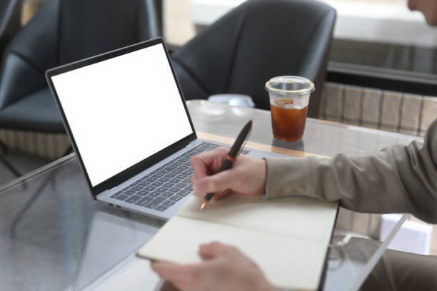 istock A close-up of a person writing in a notebook beside a laptop with an empty screen, Learning journey in a minimalist workspace, E-Learning and Digital Education concepts 2203222271