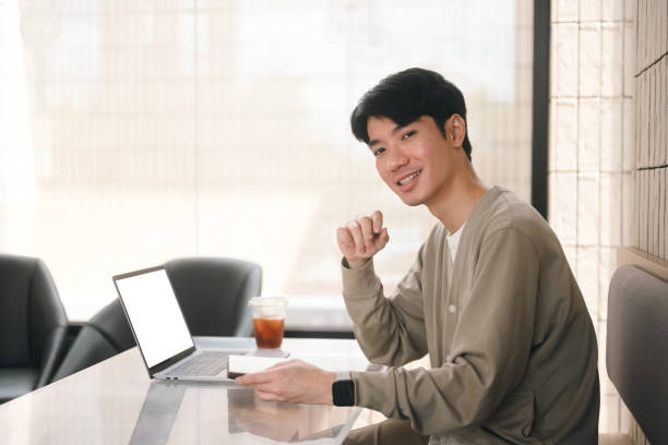 istock An Asian student sits in a modern cafe, smiling at the camera while holding a notebook and using a laptop with an empty screen, the start of an online learning session, E-Learning and Digital Education concepts 2203222441