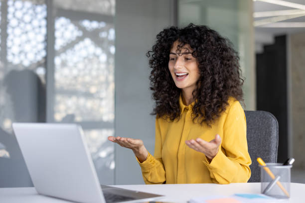 istock A woman smiles while gesturing during a vibrant video call on her laptop in a modern office setting. 2203222776