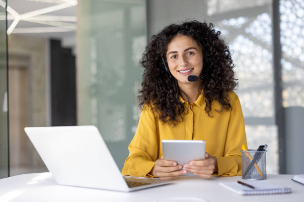istock A woman with a headset smiles warmly while holding a tablet, ready to help customers with their inquiries. 2203223162