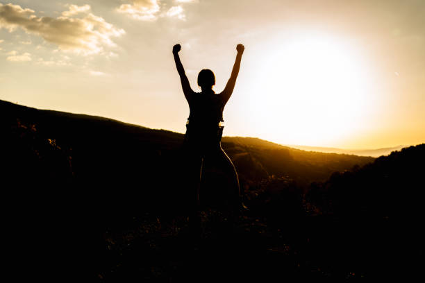 Silhouette of young hiker woman standing on a mountain top with arms outstretched