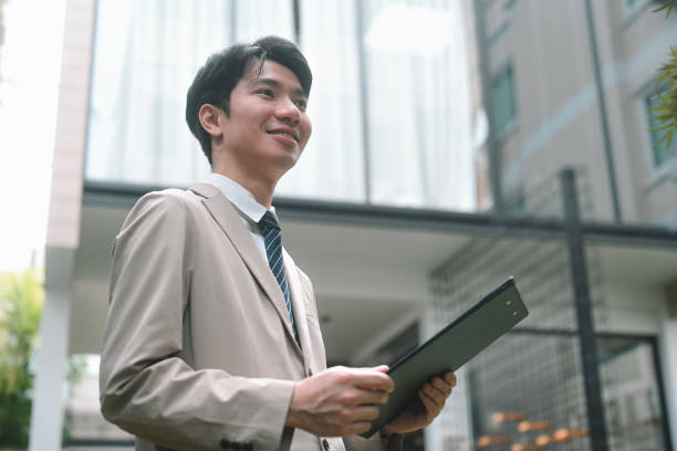 istock A young insurance agent in a formal stands confidently outdoors, holding a clipboard, with a positive and forward-looking expression, Dedicated Insurance Agent Focused on Client Satisfaction 2203223336