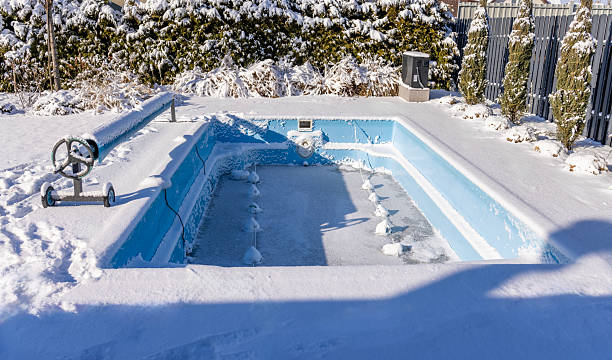 istock Empty outdoor swimming pool covered in snow during winter, surrounded by a snowy backyard with evergreen trees and a fence in the background. 2203224100