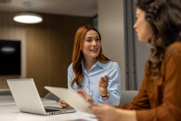 istock Businesswomen discussing paperwork in modern office using laptop 2203224183
