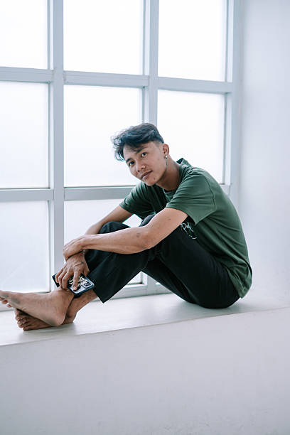 istock Relaxed young man sitting by window, holding smartphone casually 2203233137