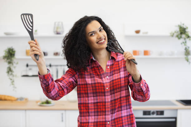 istock Smiling woman holding kitchen utensils in bright modern home kitchen interior 2203236123