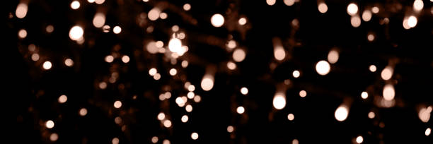 istock Blurry garland lights on a dark background. Festive Christmas and New Year background. Soft focus. Image toned in color of 2025 year - Mocha Mousse 2203236802