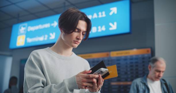 istock Crowded Airport Terminal: Young Man Scanning Plane Ticket Using Phone to Check Flight Information 2203237108