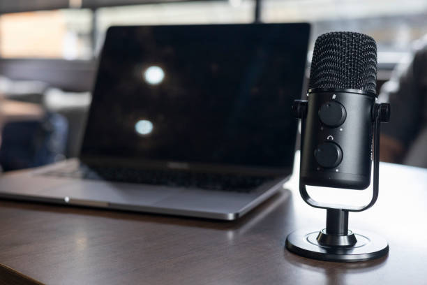istock Microphone on wooden table top view podcast studio professional audio recording equipment in minimal, Microphone sits on wooden table recording audio broadcast. Wireless earbuds quality sound music. 2203237162