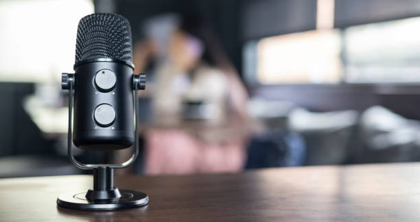 istock Microphone on wooden table top view podcast studio professional audio recording equipment in minimal, Microphone sits on wooden table recording audio broadcast. Wireless earbuds quality sound music. 2203237209