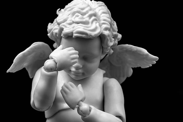 istock Sad cherub with facepalm gesturing. Angel figurine holding his head in hands on black background 2203237374