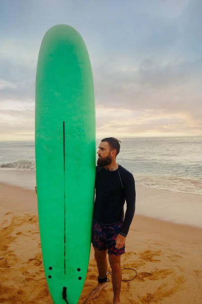 istock Young  bearded man with surfboard standing near a beach. Man with surfing board outdoors on a summer day. 2203237701