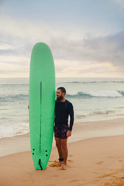 istock Young handsome male surfer with a surfboard is enjoying a view while walking a sandy beach at sea. Summer, vacation, ocean 2203237706
