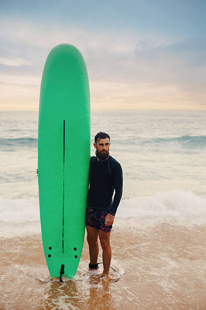 istock Young  bearded man with surfboard standing near a beach. Man with surfing board outdoors on a summer day. 2203237712