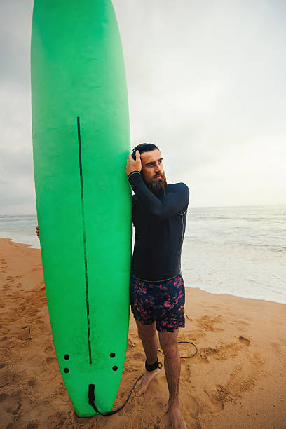istock Young  bearded man with surfboard standing near a beach. Man with surfing board outdoors on a summer day. 2203237727