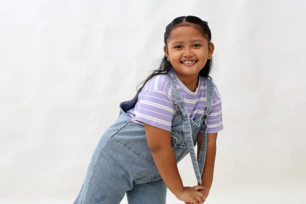 A cute portrait of an Asian toddler wearing glasses, smiling at the camera while walking down a residential street with green grass in the background in the late morning