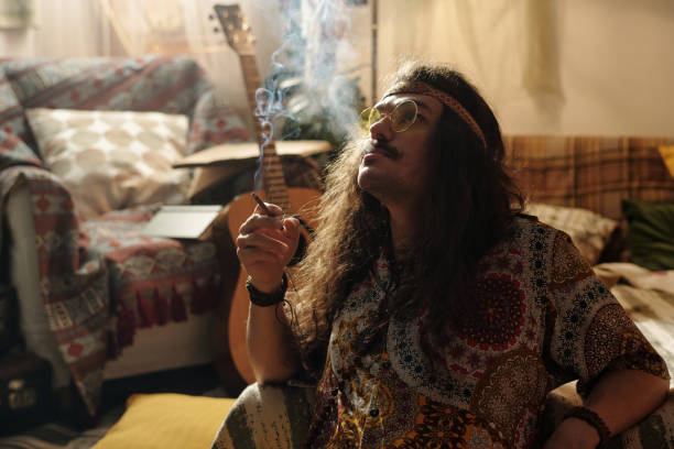 Person enjoying a moment in a cozy bohemian-styled room filled with patterned fabrics, guitar, and ambient lighting, reflecting with visible smoke from what is being smoked
