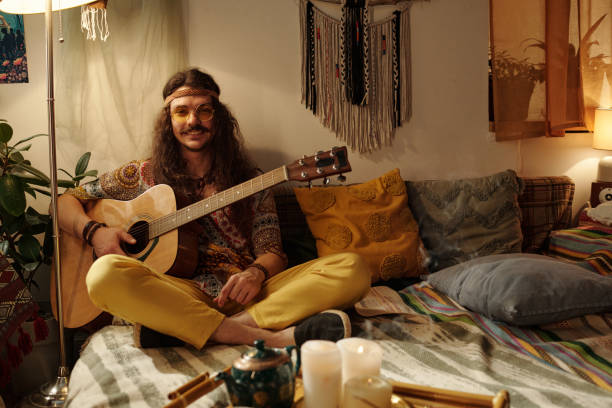 istock Smiling Young Man Playing Acoustic Guitar in Cozy Room 2203238128
