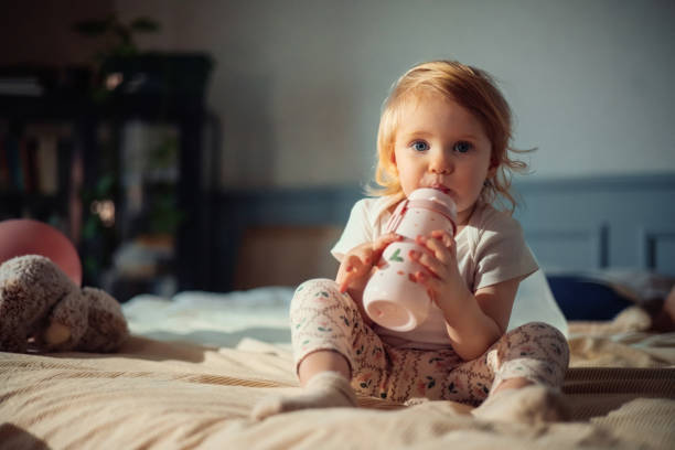 Young Child Drinking From a Bottle While Sitting on a Cozy Bed
