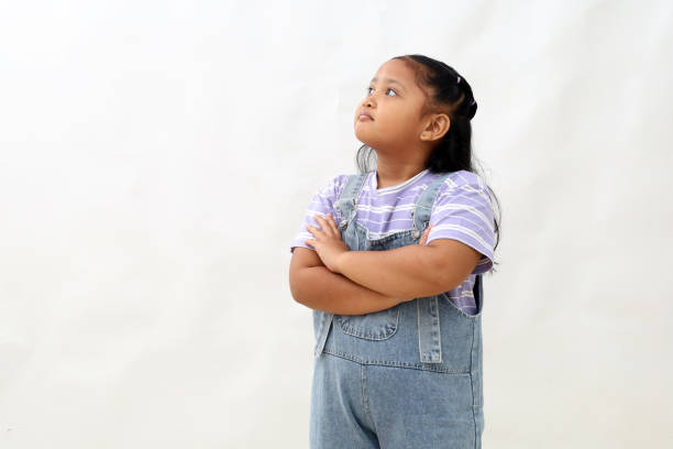 istock Happy asian little girl standing while imaging something with folded hand. Isolated on white 2203241472