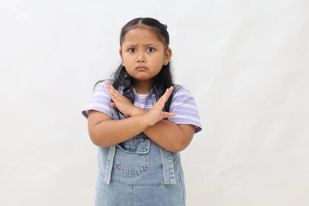 Kid crossed hands, posing stop sign, wearing red shirt on white background.