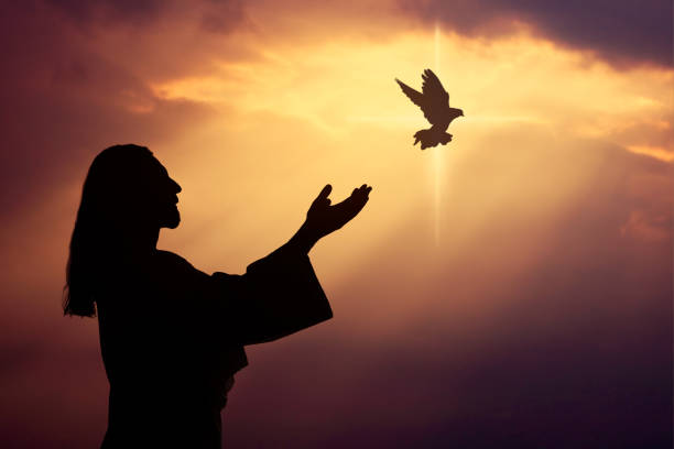 A silhouette of Jesus Christ with open hands as a dove flies toward the sky, symbolizing peace, faith, and the Holy Spirit.