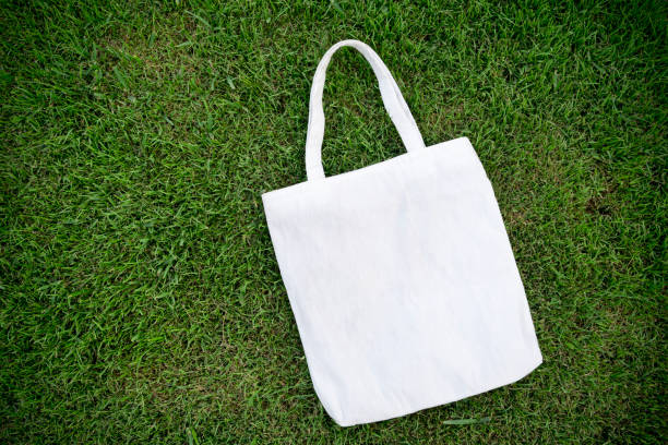 White cotton or mesh eco bag on green grass background. Zero waste, no plastic, eco friendly shopping, recycling concept. Blank mockup shopper with place for artwork or text. Flat lay, copy space