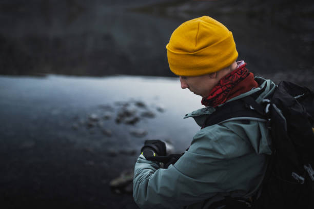 A hiker dressed warmly uses smart watch for navigation while observing lake surroundings during a mountainous outdoor adventure, underlining the beauty and tranquility of nature.