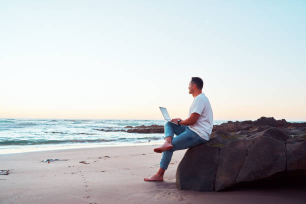 Freelancer working on laptop at beach during sunset