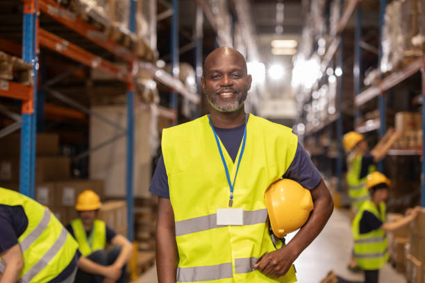 istock Smiling supervisor holding hardhat stands in warehouse with coworkers 2203257868