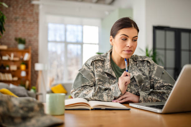 istock Young woman in military uniform working from home, focused on tasks and utilizing technology in a cozy environment 2203260174