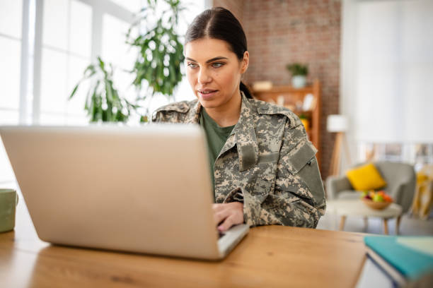 istock Young woman in military uniform working on laptop at home while managing responsibilities 2203260272