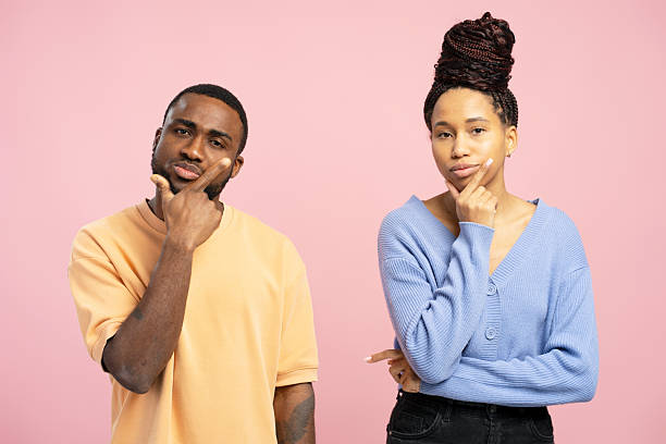 istock Pensive couple thinking and touching chin on pink background 2203262084