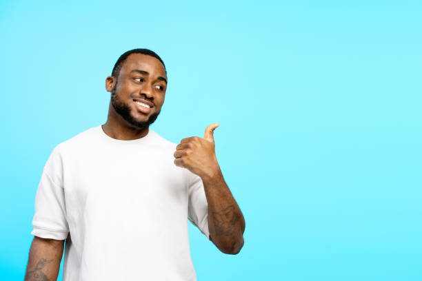 istock Young man showing thumb up and looking sideways on blue background 2203263641