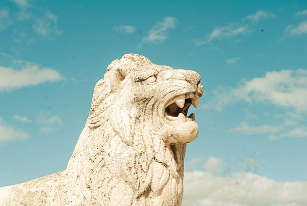 Stone lion statue roaring fiercely against a backdrop of blue sky and white clouds