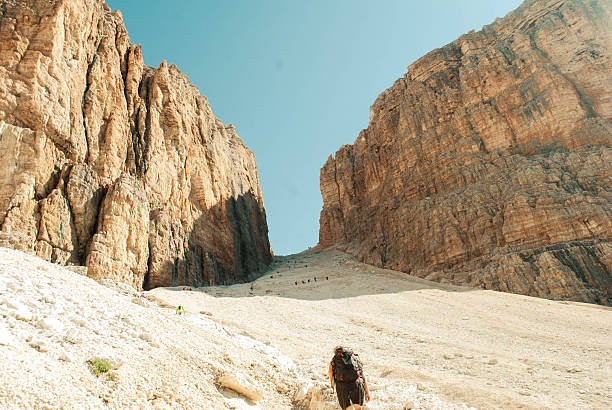 Hikers walking up a steep mountain trail between towering rock formations in the italian dolomites
