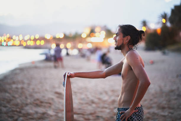 Smiling young man holding a skimboard while enjoying a beautiful sunset at the beach, relishing the moments after an exhilarating skimboarding session on the shore