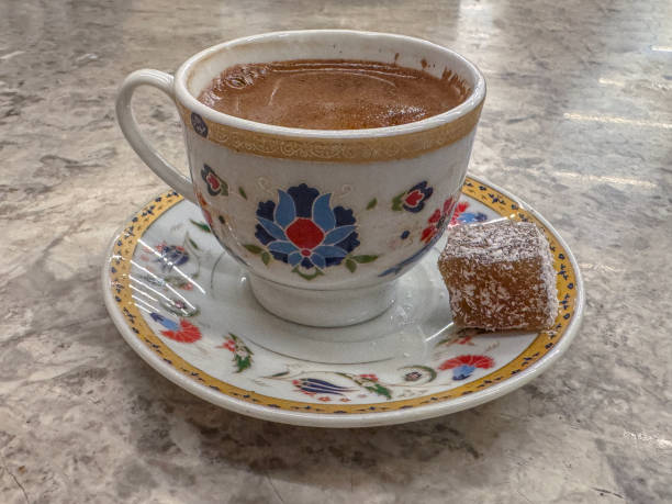 A beautifully painted floral cup containing traditional Turkish coffee, accompanied by a piece of Turkish delight served on a detailed decorative saucer