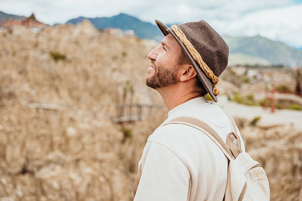 Bearded man in a hat smiling at rocky formations. Traveler appreciating nature's beauty. Adventure and exploration in outdoor natural settings.