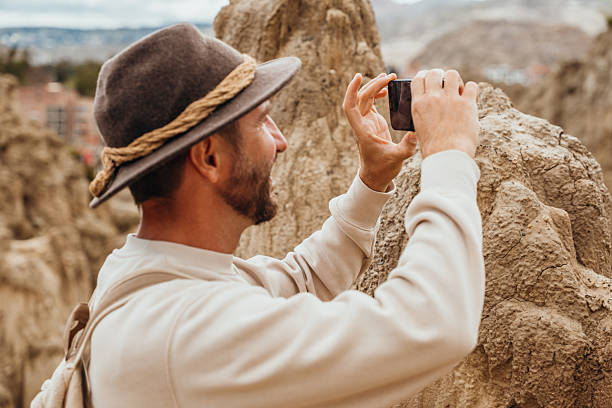 Man with backpack photographing rugged rock formations outdoors. Tourist exploring scenic mountainous terrain. Adventure travel and nature photography.