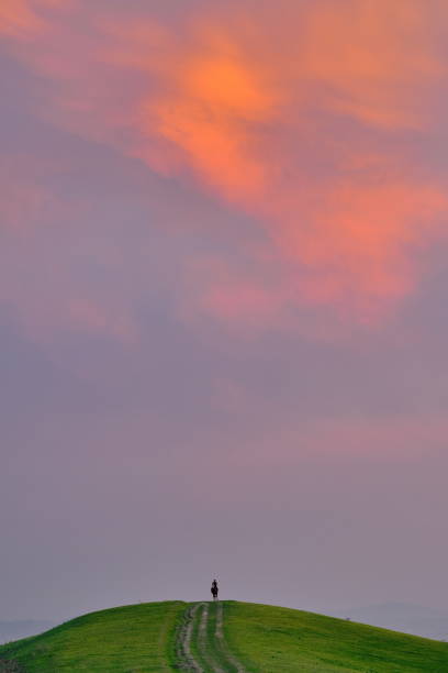 istock A lone rider on a grassy hill under a vibrant sunset sky with soft clouds, in a serene landscape. Kyrgyzstan. 2203276745